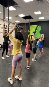 אימון ילדים בברפיט יבנה – ילדים מרימים משקולות מעל הראש עם המאמנת